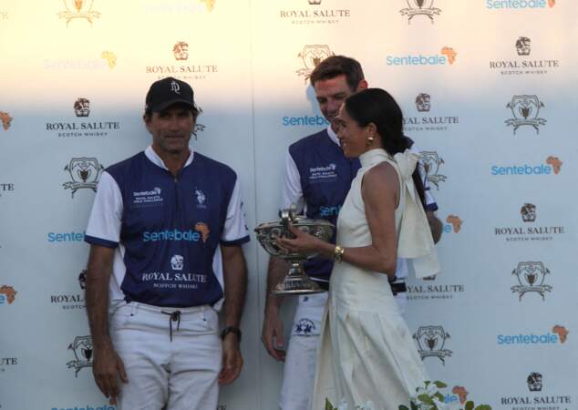La duchesse de Sussex présente le trophée à son mari, le duc de Sussex, après la victoire de son équipe, la Royal Salute Sentebale Team, sur la Grand Champions Team.